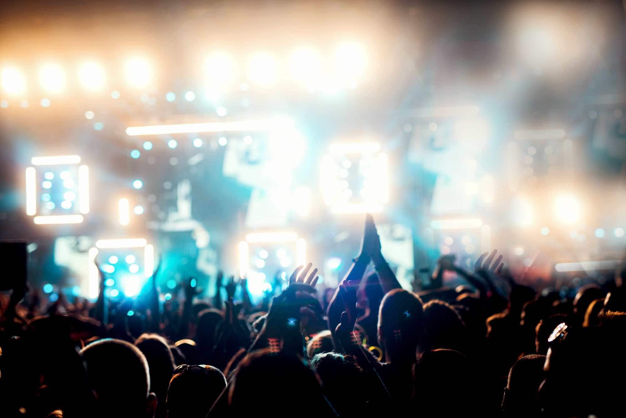 Crowd people at music festival concert holding hands up near stage